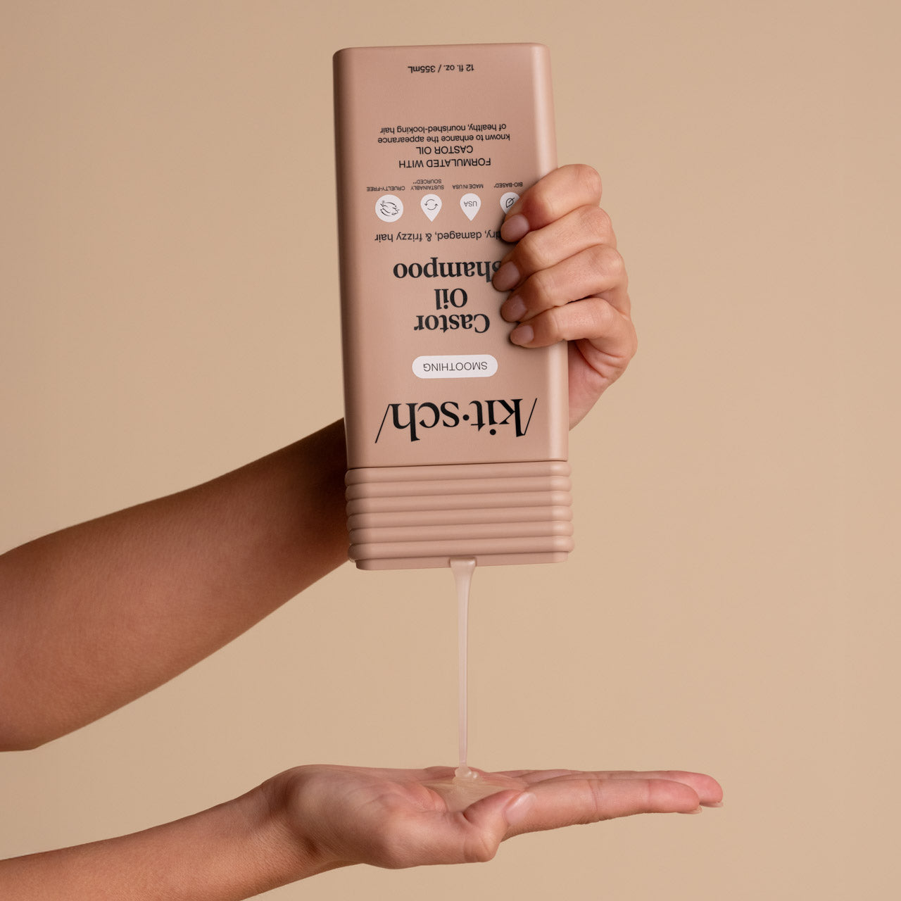 Hand dispensing KITSCH Castor Oil Nourishing Shampoo from bottle into palm on a beige background